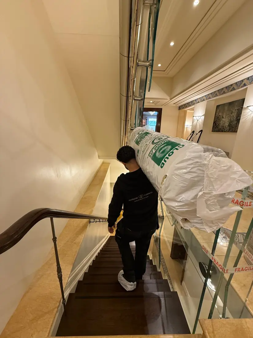 Supreme Carpets fitter carrying flooring up a staircase