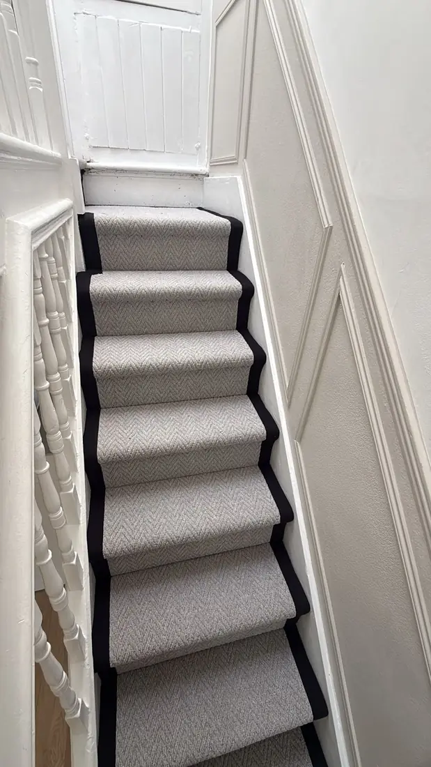 Narrow staircase with a grey runner and black whipped edges